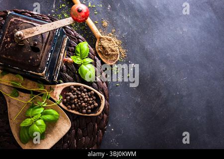 Alte Mühle und Holzlöffel mit Gewürzen auf einem schwarzen Tisch Stockfoto