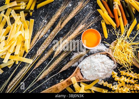 Rohe Teigwaren, Mehl und andere Produkte auf einem schwarzen, strukturierten Tisch Stockfoto
