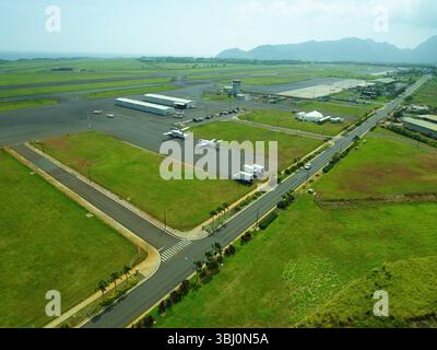 Luftbild eines Flugplatzes in Kauai mit mehreren Start- und Landebahnen, Rollbahnen, kleinen Flugzeugen, Terminalstrukturen und riesigen grünen Feldern mit dem fernen Ozean A Stockfoto