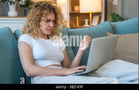 Junge Frau, die von zu Hause aus auf einem Laptop arbeitet und technische Probleme wie Internetunterbrechung, Computerfehler oder Systemfehler hat, frustriert und Stockfoto