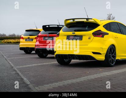 Rückstände von zwei gelben Fokus-ST und einem roten Fokus-RS, die auf einem leeren Parkplatz geparkt sind. Hintere Dreiviertelansicht von drei Ford-Fließhecken. Stockfoto