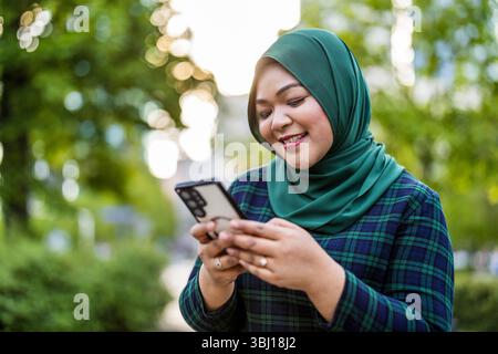 Porträt einer jungen muslimischen Frau, die im Freien das Handy benutzt Stockfoto