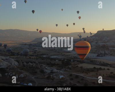 Ein magischer Drohnenfoto des Sonnenaufgangs über Göreme, während bunte Heißluftballons abheben und den Himmel über der surrealen kappadokischen Landschaft in Gold malen Stockfoto