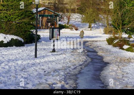 Jemand läuft allein auf einem eisigen Pfad in einem Winterpark in Harrogate, Yorkshire, Großbritannien. Stockfoto