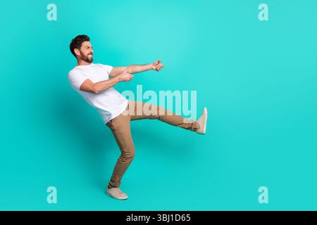 Junger Mann mit lebhaften Gesten vor türkisfarbenem Hintergrund, stilvoll mit weißem Hemd und brauner Hose gekleidet Stockfoto