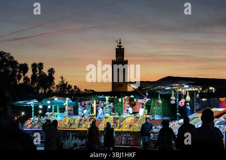 Marrakesch, Marokko - 20. Februar 2025: Touristen schlendern um den Stand auf dem berühmten Platz Jemaa el-Fnaa mit dem Minarett Koutoubia in Marrakesch Stockfoto