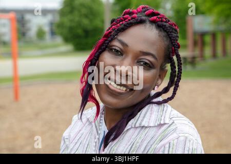Porträt einer glücklichen jungen Schwarzen Frau mit violetten Zöpfen, die ein gestreiftes Hemd tragen und selbstbewusst in die Kamera lächeln Stockfoto