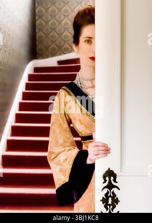 Eine Frau in einem Vintage-Kleid blickt hinter einer weißen Tür heraus, mit einer Treppe im Hintergrund. Stockfoto