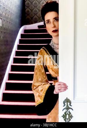 Eine Frau in einem Vintage-Kleid blickt hinter einer weißen Tür heraus, mit einer Treppe im Hintergrund. Stockfoto