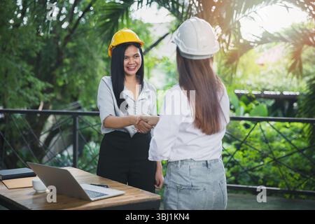 Zwei asiatische Architektin und Ingenieurin in Schutzhelmen, die nach dem Treffen die Hand schütteln. Konzept der erfolgreichen Zusammenarbeit. Stockfoto