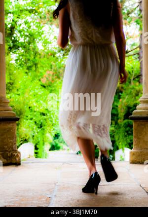 Eine Frau in weißem Kleid und schwarzen Absätzen läuft von der Kamera weg. Stockfoto