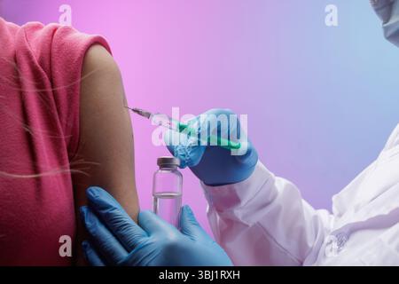 Arzt in Handschuhen, die einem Patientenarm mit einer Spritze eine Impfstoffinjektion geben, wobei er die Gesundheitsfürsorge, den Schutz und den Immunisierungsprozess hervorhebt. Stockfoto