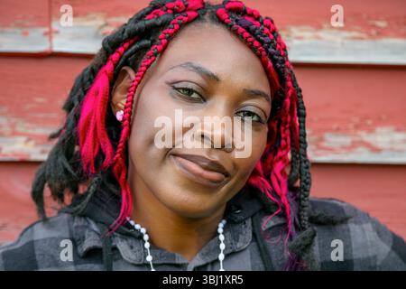 Selbstbewusste afroamerikanische Frau mit farbenfroher schützender Frisur, Kapuzenpullover, urbanes Lifestyle-Porträt mit Backsteinmauern Stockfoto