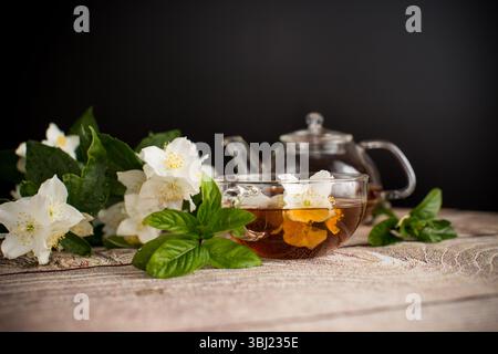 Duftender Tee mit Jasminblüten in einer Glasschale auf schwarzem Hintergrund. Stockfoto