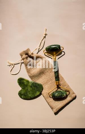Hautpflegewerkzeuge flach gelegt: gua-Sha-Schaber und Jadewalze auf Beige. Ideal für zu Hause Gesichtsmassagen und natürliche Schönheitsroutinen Stockfoto