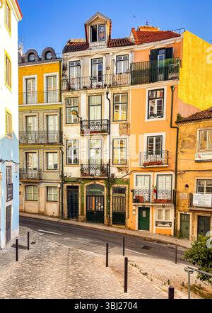 Farbenfrohe traditionelle portugiesische Gebäude mit schmiedeeisernen Balkonen säumen eine enge Kopfsteinpflasterstraße im historischen Lissabon, Portugal, Europa. Stockfoto