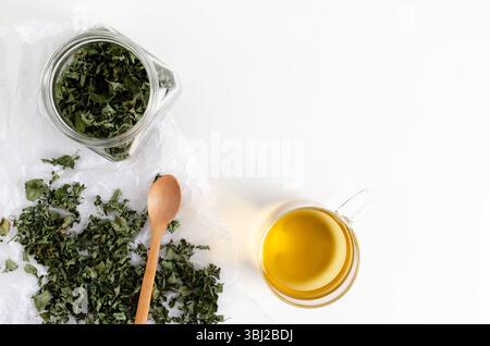 Eine Tasse Pfefferminztee und getrocknete Minzblätter in einem Glas und auf weißem Papier, auf weißem Hintergrund. Draufsicht. Stockfoto