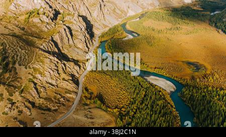Aus der Vogelperspektive auf ein malerisches Bergtal mit einem sich windenden Fluss, der durch üppige Wälder fließt, und einer Straße, die sich entlang schlängelt und eine atemberaubende Herbstlandschaft schafft Stockfoto