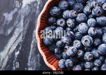 Frische Heidelbeeren in roter Schüssel. Saftige Bio-Früchte auf schwarzem Marmor. Sommer Antioxidans Superfood. Leckere süße Beeren. Gesunde Dessert Nahaufnahme. Stockfoto