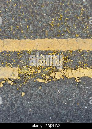 Beschädigte doppelte gelbe Linien. Fahrbahnmarkierungen, die reparaturbedürftig sind, oder vielleicht eine Metapher für Grenzüberschreitungen oder Regeln Stockfoto