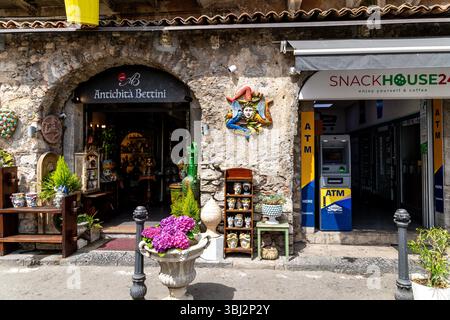Taormina, Sizilien - Italien - 05-04-2025: Straßenblick in Taormina, Sizilien mit Antiquitätenladen Antichità Bettini, farbenfrohen Keramiken, Pflanzen und Geldautomaten nex Stockfoto