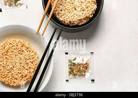 Rohe Instantnudeln in Schüsseln mit Stäbchen und Gewürzen auf weißem Grunge-Hintergrund Stockfoto