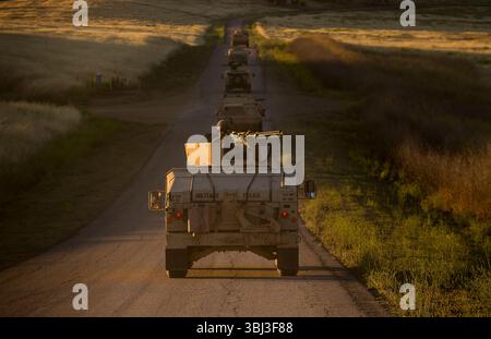 Ein HMMWV-Konvoi der US Army fährt bei Sonnenaufgang in gerader Linie durch stimmungsvolles, sandiges und einsames Gelände und ruft Themen der Bereitschaft und Widerstandsfähigkeit hervor. Stockfoto