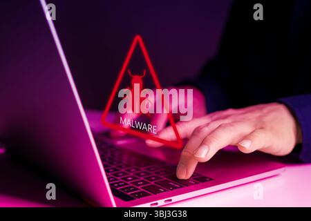 Das Warnsymbol für digitale Malware wird auf dem Bildschirm angezeigt, während der Benutzer an einem Laptop arbeitet. Es zeigt Cyberbedrohungen, Virenangriffe, Hackerrisiken und Online-Angriffe an Stockfoto