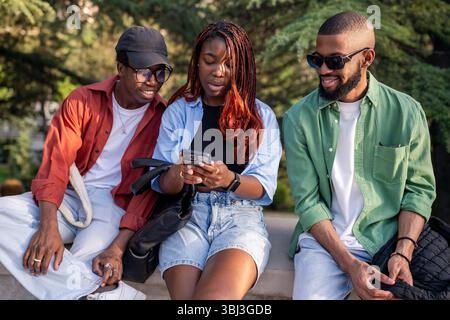 Lebhafter afroamerikanischer Freund sitzt im Park, Telefon in der Hand. Frau teilt trendige Social-Media-Beiträge Stockfoto