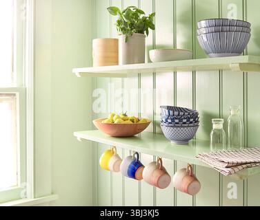Offene Küchenregale mit farbenfrohen Tassen, Schüsseln und frischem Obst Stockfoto