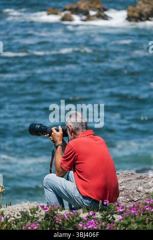 Mann in blauer Jeans und rotem T-Shirt, Fotograf mit Kamera, der das Meer fotografiert Stockfoto