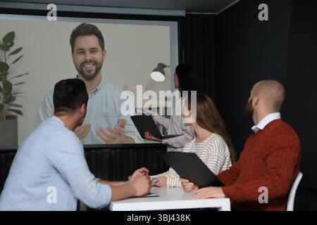 Gruppe von Personen, die an einer Geschäftskonferenz im Innenbereich teilnehmen. Lautsprecher auf Projektionsleinwand Stockfoto