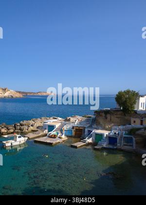 Klippen und traditionelle Fischerhütten von Mandrakia unter strahlender Sonne. Türkisfarbenes Meer steht im Kontrast zu weißen Fassaden und lebhaften Küstenstrukturen. Stockfoto