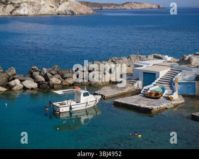 Kleines Boot am langen Steinpier in der Mandrakia Bay, Milos, mit ein paar weißen Hütten und der offenen Ägäis unter klarem sonnigem Himmel. Stockfoto