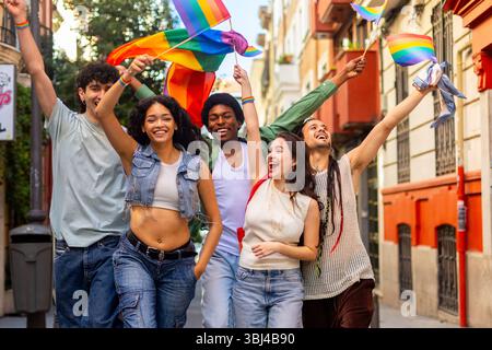 Eine Gruppe fröhlicher, multirassischer Menschen, die die Straße hinunterlaufen und Regenbogenfahnen schwenken, um den Stolz der Schwulen zu feiern Stockfoto
