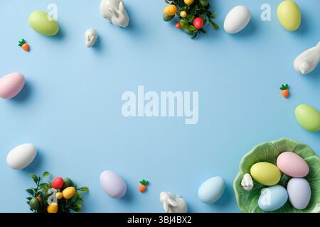 Happy Easter-Konzept. Rahmen von oben mit pastellfarbenen Ostereiern, Keramikhasen, Karotten, Dekorationen auf blauem Hintergrund Stockfoto
