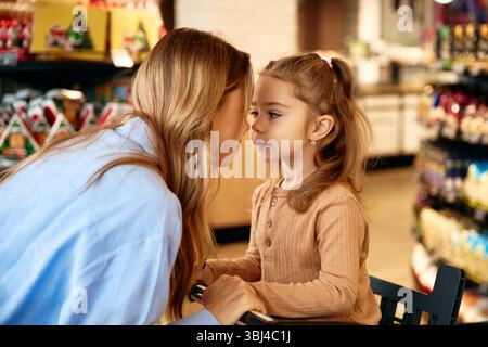 Zärtlicher Moment zwischen Mutter und Tochter, die beim Einkaufen im Lebensmittelgeschäft die Stirn berühren. Warmes Licht und festliche Dekoration im Hintergrund. Familie Stockfoto