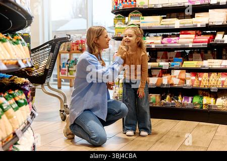 Zärtlicher spielerischer Moment zwischen Mutter und Tochter im Lebensmittelgeschäft. Mutter berührt sanft die Nase der Tochter, lächelt und bindet sich während des Essens. F Stockfoto