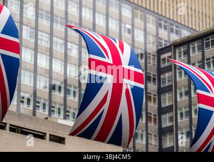 Aus nächster Nähe sehen Sie mehrere große Flaggen mit dem Design von Union Jack, die vor dem Hintergrund moderner Gebäude in London mit gl sichtbar sind Stockfoto