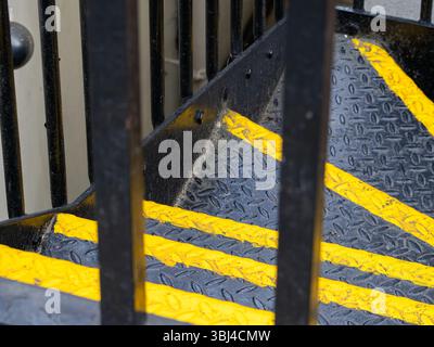 Nahaufnahme einer Treppe mit gelben Sicherheitsstreifen und Metallgeländern. Die Treppen haben eine strukturierte Oberfläche, die Grip und Sicherheit erhöht. Industria Stockfoto