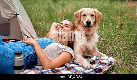 Eine fröhliche Frau entdeckt tiefe Ruhe beim Campen im Freien, schwelgt in der Gesellschaft ihres verspielten Golden Retriever und schätzt die besondere Bindung, die sie hegen Stockfoto