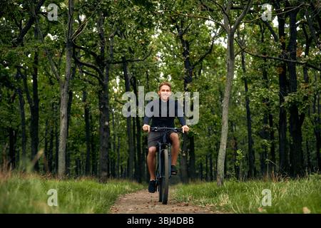Ein fröhlicher und fröhlicher Mann fährt energisch mit seinem Mountainbike auf einem wunderschönen malerischen Weg, der sich durch einen lebendigen grünen Wald schlängelt, ganz ich Stockfoto