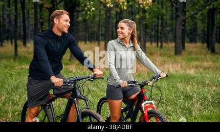 Ein fröhliches Paar auf Mountainbikes lächelt sich an und genießt eine aufregende Fahrt durch einen wunderschönen Wald, die das Wesen des Outdoor adve unterstreicht Stockfoto