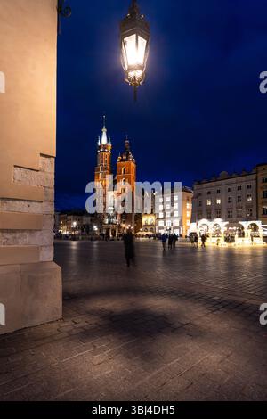 Krakau, Polen: Touristen und Einheimische spazieren vor der Marienkirche auf dem Marktplatz namens Rynek Glowny in der Krakauer Altstadt in der Dämmerung. Stockfoto