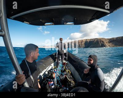 Taucher bereiten ihre Ausrüstung auf einem Schlauchboot vor und segeln in Richtung Küste für einen Tauchausflug Stockfoto