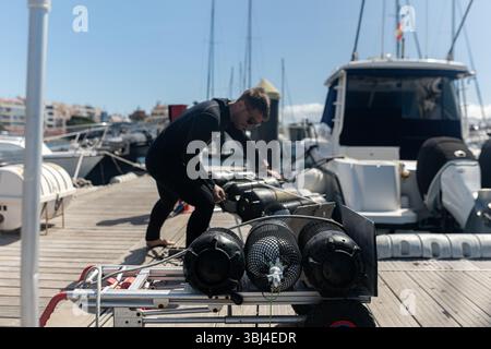 Professioneller Taucher sichert Tauchbecken auf einem Wagen am Yachthafen und macht sich bereit für einen Tauchgang Stockfoto