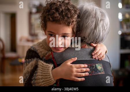 Glückliches Enkelkind, das Großmutter zu Hause zärtlich umschließt und einen Moment der Zuneigung und Liebe genießt Stockfoto