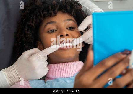 Zahnarzt zeigt perfekte Zähne, während der lächelnde Patient in einer einladenden Zahnklinik anschaut, wobei er auf Mundgesundheit und Hygiene hinweist Stockfoto
