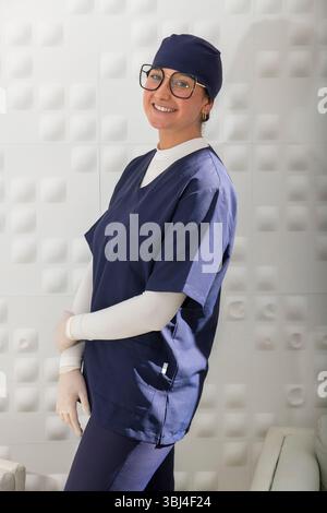 Porträt einer selbstbewussten Zahnärztin, die lächelnd in Uniform und Handschuhen ist, bereit, Patienten in einer modernen, hellen Zahnklinik zu helfen Stockfoto
