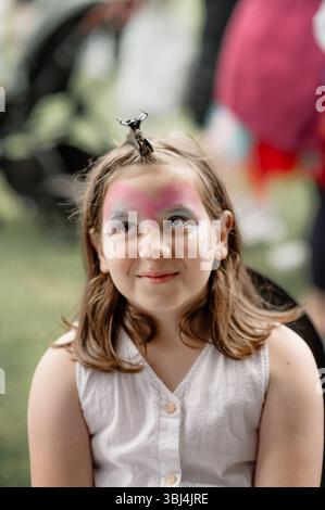 Lächelndes Mädchen, das auf den nächsten Teil ihres Gesichtsgemäldes wartet. Stockfoto